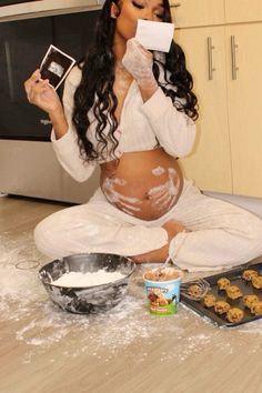 a pregnant woman sitting on the kitchen counter with cookies and cupcakes in front of her