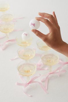 a hand holding an egg in front of several wine glasses with pink bows on them