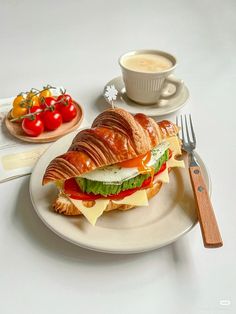 a sandwich on a white plate next to a cup of coffee and some cherry tomatoes