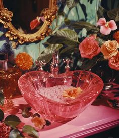 a pink sink sitting on top of a table next to flowers