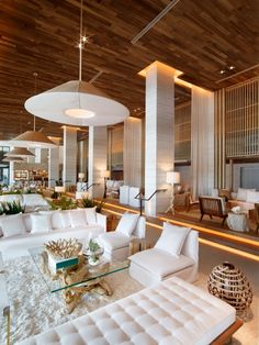 a living room filled with white furniture next to a tall wooden ceiling above a fire place