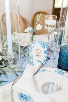 the table is set with blue and white plates, silverware, candles and flowers