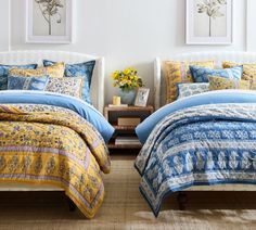 two beds with blue and yellow comforters in a room next to paintings on the wall