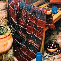 a blanket is hanging on a wooden bench next to two mugs and a potted plant