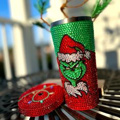 a green and red cup sitting on top of a wooden bench next to a plant