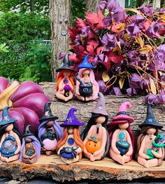 many small figurines are sitting on a piece of wood with purple flowers in the background