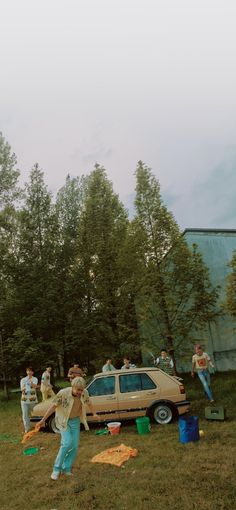 a group of people standing on top of a grass covered field next to a car