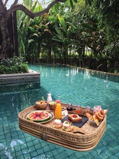 a wicker tray with food on it sitting next to a pool in the middle of a jungle