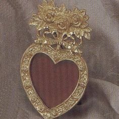 a heart shaped brooch sitting on top of a piece of cloth covered in gold thread