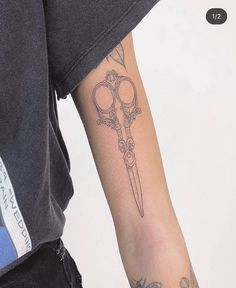 a person with a tattoo on their arm holding a pair of scissors in one hand