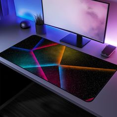 a computer desk with a monitor, keyboard and mouse on it in front of a colorful background