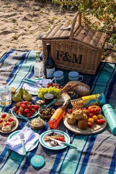 a picnic blanket with food and drinks on it, including breads, fruit, crackers, and wine bottles