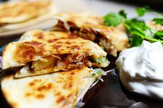 two quesadillas on a plate with sour cream and cilantro garnish