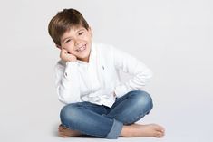 a young boy sitting on the floor with his hands behind his head and smiling at the camera