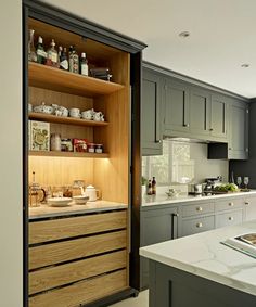 an open cabinet in the middle of a kitchen with white counter tops and gray cabinets