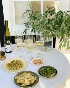 a table topped with plates of food and glasses of wine next to a potted plant