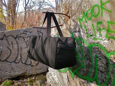 a black duffle bag hanging on a wall with green spray painted graffiti in the background