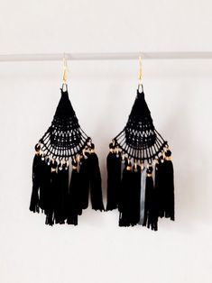 two pairs of black tasseled earrings hanging from a clothes line against a white wall