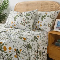 a bed with white sheets and yellow flowers on it, next to a wooden night stand