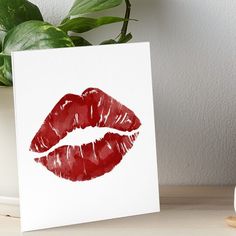 a white card with a red lipstick print on it next to a potted plant