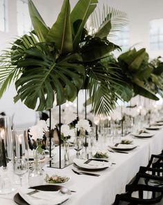 the table is set with black and white plates, silverware, greenery and candles