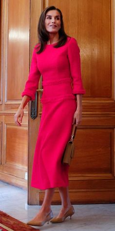 a woman in a pink dress is standing by a door