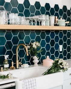 a kitchen with blue tiles and white flowers on the counter top next to a sink