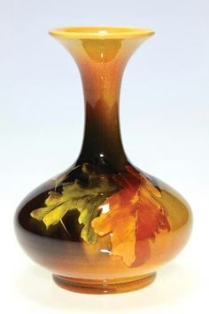 a brown and yellow vase with leaves on it's sides, sitting against a white background