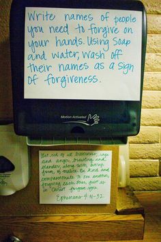 a handwritten note attached to a sign on a wooden desk next to a paper towel dispenser