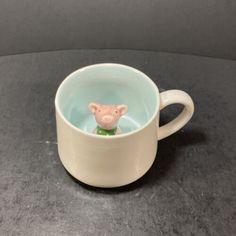 a small toy pig in a coffee cup on a black counter top with grey background