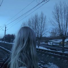 a woman with long blonde hair standing on train tracks in the snow at night time