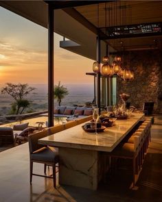 an outdoor dining area overlooking the ocean and mountains at sunset with hanging lights on the ceiling