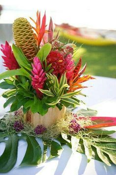 an arrangement of tropical flowers and greenery is displayed on a table at a wedding