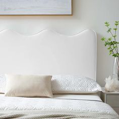 a bed with white sheets and pillows in a bedroom next to a painting on the wall