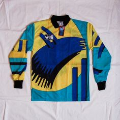 a blue and yellow shirt with an image of a bird on the front is laying on a white sheet