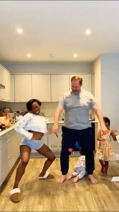 a man and two young children dancing in a kitchen with an adult standing next to them