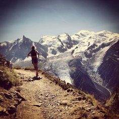 a man is running on a trail in the mountains with snow covered mountains behind him