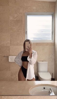 a woman taking a selfie in front of a bathroom mirror