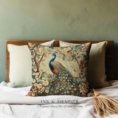 a peacock pillow on top of a bed next to two pillows with tassels