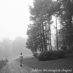 a person walking down a dirt road in the woods on a foggy, overcast day