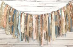 an assortment of different colored ribbons hanging from a string on a white wooden wall with wood planks in the background