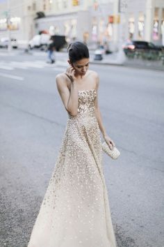 a woman in a long dress is talking on her cell phone while walking down the street