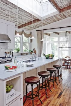 a kitchen with wooden floors and white cabinets, an island countertop and stools