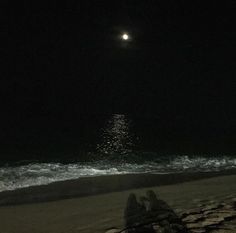 two people are sitting on the beach at night