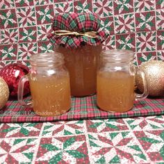 three mason jars filled with apple cider sitting on a plaid tablecloth next to christmas ornaments