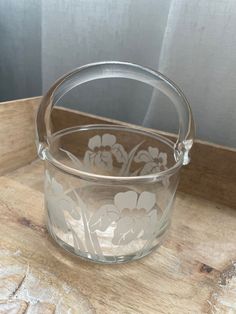 a clear glass container with white flowers on the inside and bottom, sitting on a wooden surface