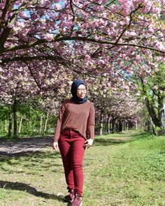 a woman standing in front of a tree with pink flowers on it's branches