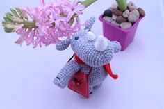 a small stuffed elephant holding a pink flower in its trunk next to a potted plant