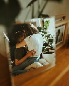 a man and woman hugging each other in front of a mirror with plants behind them