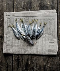 some fish are laying on top of a newspaper and placed on a wooden surface,